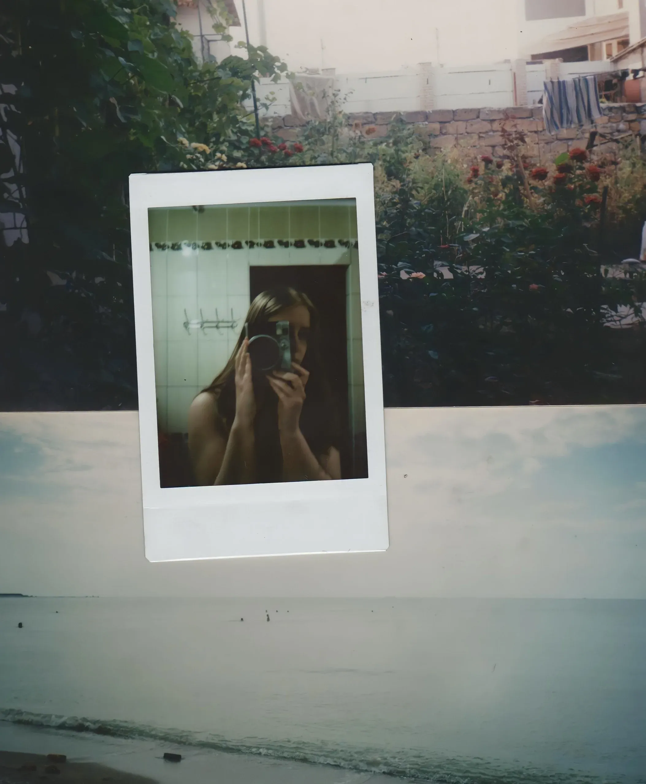 A polaroid self-portrait held over a photo of the sea